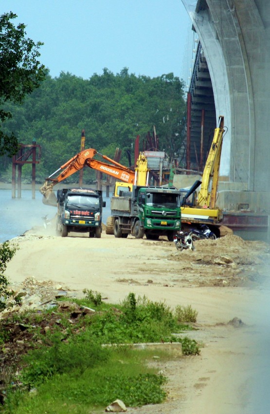 Hàng loạt xe tải mang logo xe Tân Đức được hai chiếc máy xúc cỡ lớn tiến hành múc cát và đất tại hợp phần dự án đường công vụ phía dưới chân cầu Bến Rừng.