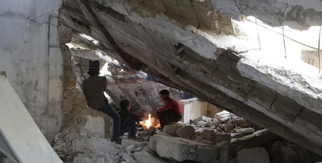 Những b&eacute; trai sưởi ấm b&ecirc;n đống lửa dưới một to&agrave; nh&agrave; đổ n&aacute;t tại tỉnh Idlib, Syria, ng&agrave;y 29/12/2015. Ảnh:&nbsp;Reuters.