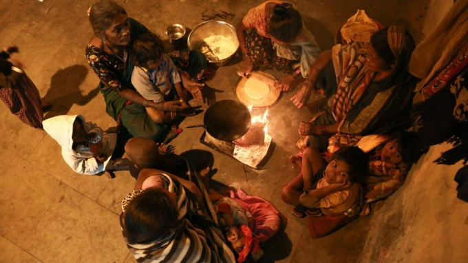 Một nh&oacute;m những người v&ocirc; gia cư gồm phụ nữ v&agrave; trẻ em đang nấu bữa tối quanh đống lửa. (Ảnh: AMAL KS/HT)