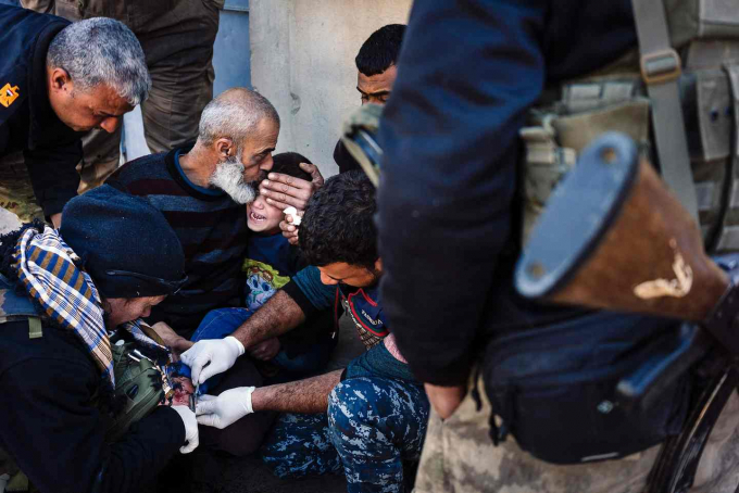 Một người Iraq cao tuổi an ủi một cậu b&eacute; bị thương v&agrave; đang được điều trị bởi lực lượng y tế trong một khu phố tại