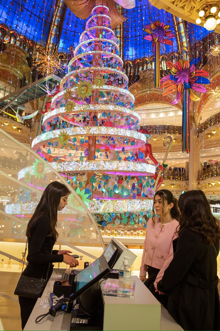 Quầy bán hàng hiệu bên cây thông Noel chính của thành phố Paris với chiều cao 21 mét mang trên mình những đồ chơi mang tính biểu tượng và ông già Noel nằm trong TTTM Galeries Lafayette.