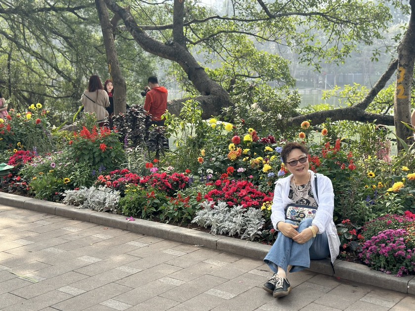 Du khách chụp ảnh lưu niệm cùng vườn hoa xuân bên hồ Gươm.