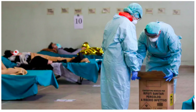 Các nhân viên mang theo một hộp chất thải y tế nguy hiểm khi bệnh nhân nằm trên giường chờ tạm được lắp đặt khẩn cấp để giảm bớt các thủ tục tại bệnh viện Brescia ở miền bắc Italy. (Luca Bruno / The Associated Press)