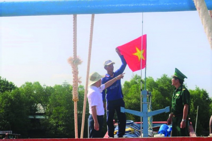 Phó Tổng biên tập Trần Đức Vinh (bìa trái) và đại diện BĐBP Kiên Giang cùng ngư dân treo cờ trên nóc tàu cá.