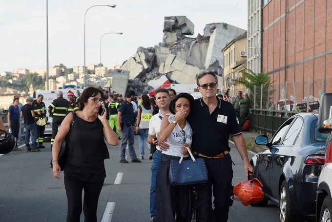 Một người l&iacute;nh cứu hỏa d&igrave;u một phụ nữ đang bật kh&oacute;c v&igrave; sợ h&atilde;i ra ngo&agrave;i sau khi chứng kiến vụ sập cầu kinh ho&agrave;ng tại th&agrave;nh phố Genoa, Italy. Ảnh: Reuters