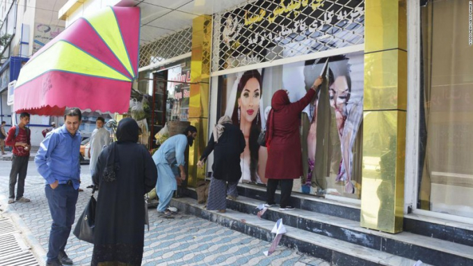 Các công nhân tại một thẩm mỹ viện ở Kabul bóc những tấm ảnh lớn có hình phụ nữ vào ngày 15/8/2021. (Ảnh: CNN)