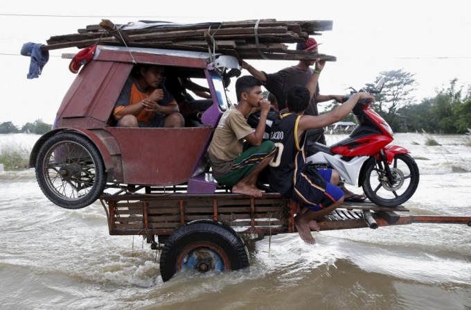 Người d&acirc;n v&agrave; phương tiện được một chiếc xe ba b&aacute;nh chở đi qua những đoạn ngập nước do ảnh hưởng của một cơn b&atilde;o đổ bộ v&agrave;o miền bắc Philippines năm 2015. (Ảnh: Reuters)