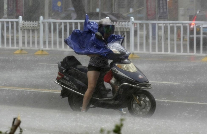Một c&ocirc; g&aacute;i mặc &aacute;o mưa v&agrave; đội mũ bảo hiểm để chống lại cơn mưa xối xả tạt v&agrave;o mặt do ảnh hưởng của b&atilde;o&nbsp;Rammasun v&agrave;o tỉnh Quảng Đ&ocirc;ng, Trung Quốc năm 2014. (Ảnh: Reuters)