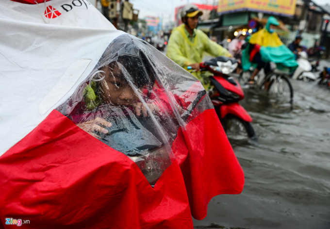 L&uacute;c n&agrave;y trời vẫn mưa lất phất, một học sinh được phụ huynh che chắn cẩn thận khi cố gắng dắt xe qua đường ngập.