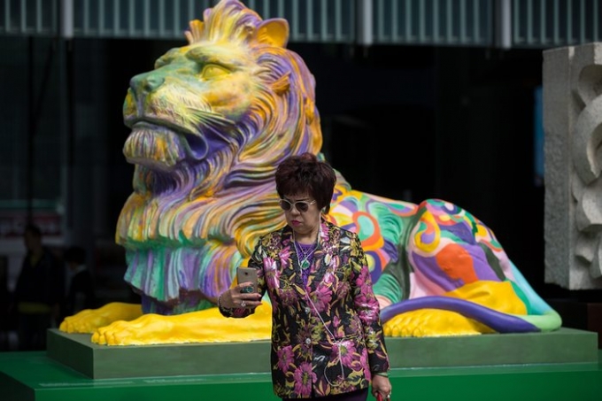 Người phụ nữ chụp ảnh b&ecirc;n cạnh bản sao của bức tượng sư tử nổi tiếng HSBC sơn m&agrave;u cầu vồng b&ecirc;n ngo&agrave;i Ng&acirc;n h&agrave;ng trung ương tại Hồng K&ocirc;ng, Trung Quốc. (Nguồn: EPA)