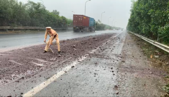 Phát hiện đất rơi vãi kéo dài trên đại lộ Thăng Long, CSGT Hà Nội dừng xe phân luồng và dọn đất dưới mưa