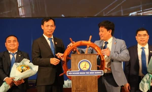 Ông Võ Sơn Điền (bìa phải) và ông Huỳnh Trần Phi Long (bìa trái) trên biểu tượng bánh lái con thuyền Hội Doanh nhân trẻ Bình Dương.